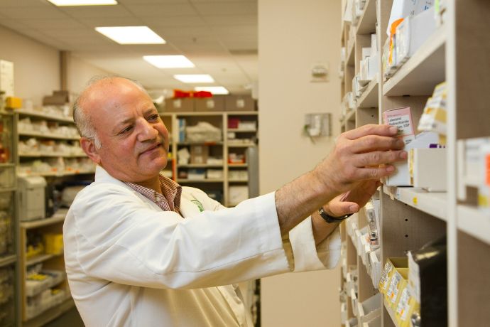 A male pharmacist is selecting a drug from a display case in a pharmacy
